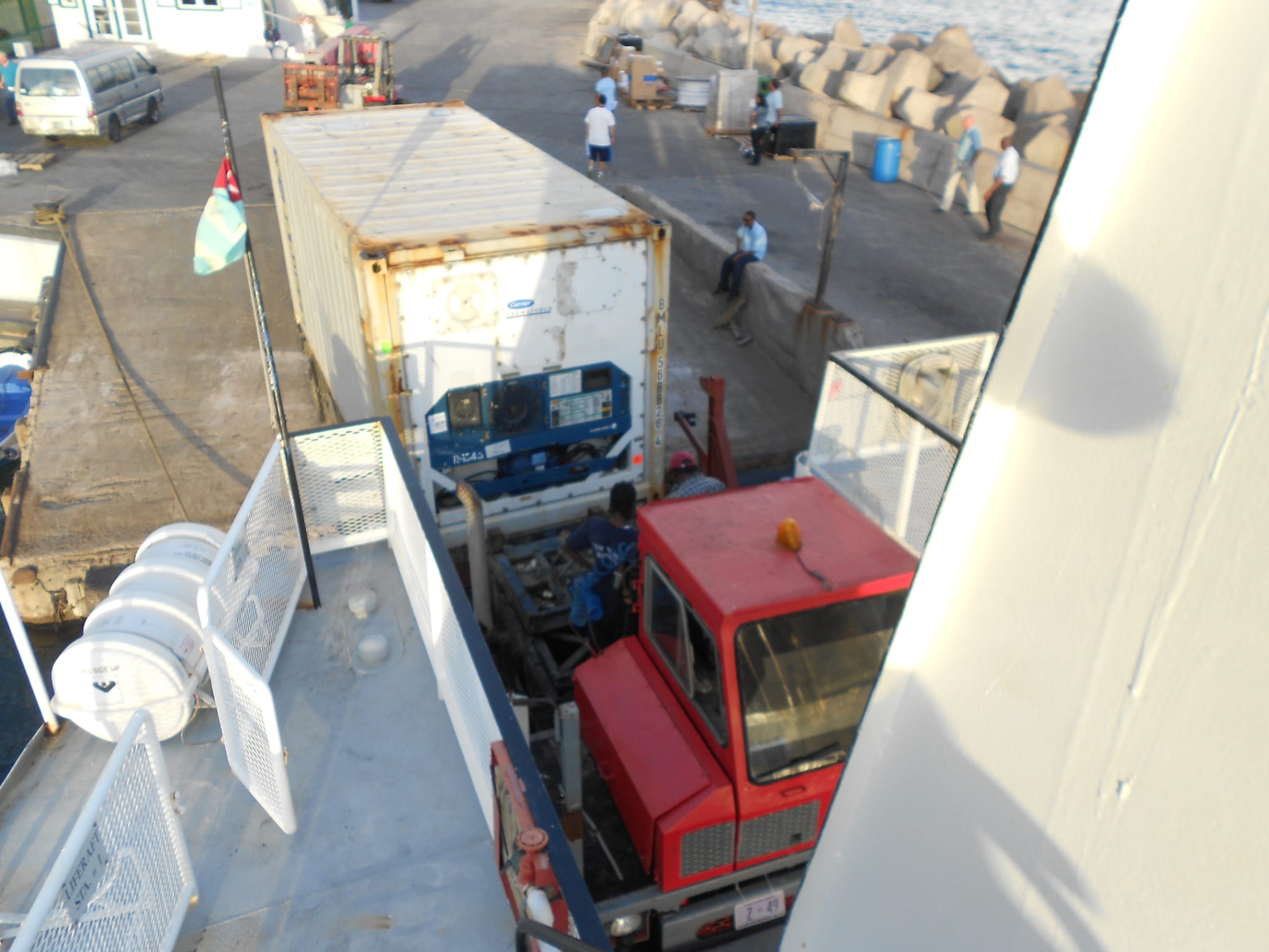 Contenedor refrigerado descargado de un barco sobre un camión en el muelle, con operarios trabajando