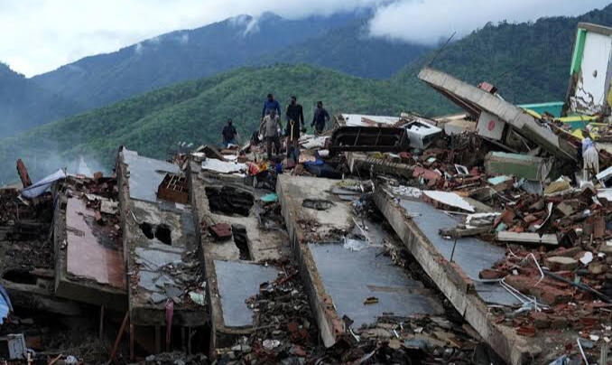 Personas trabajando sobre los escombros de edificios colapsados tras el terremoto, con montañas al fondo